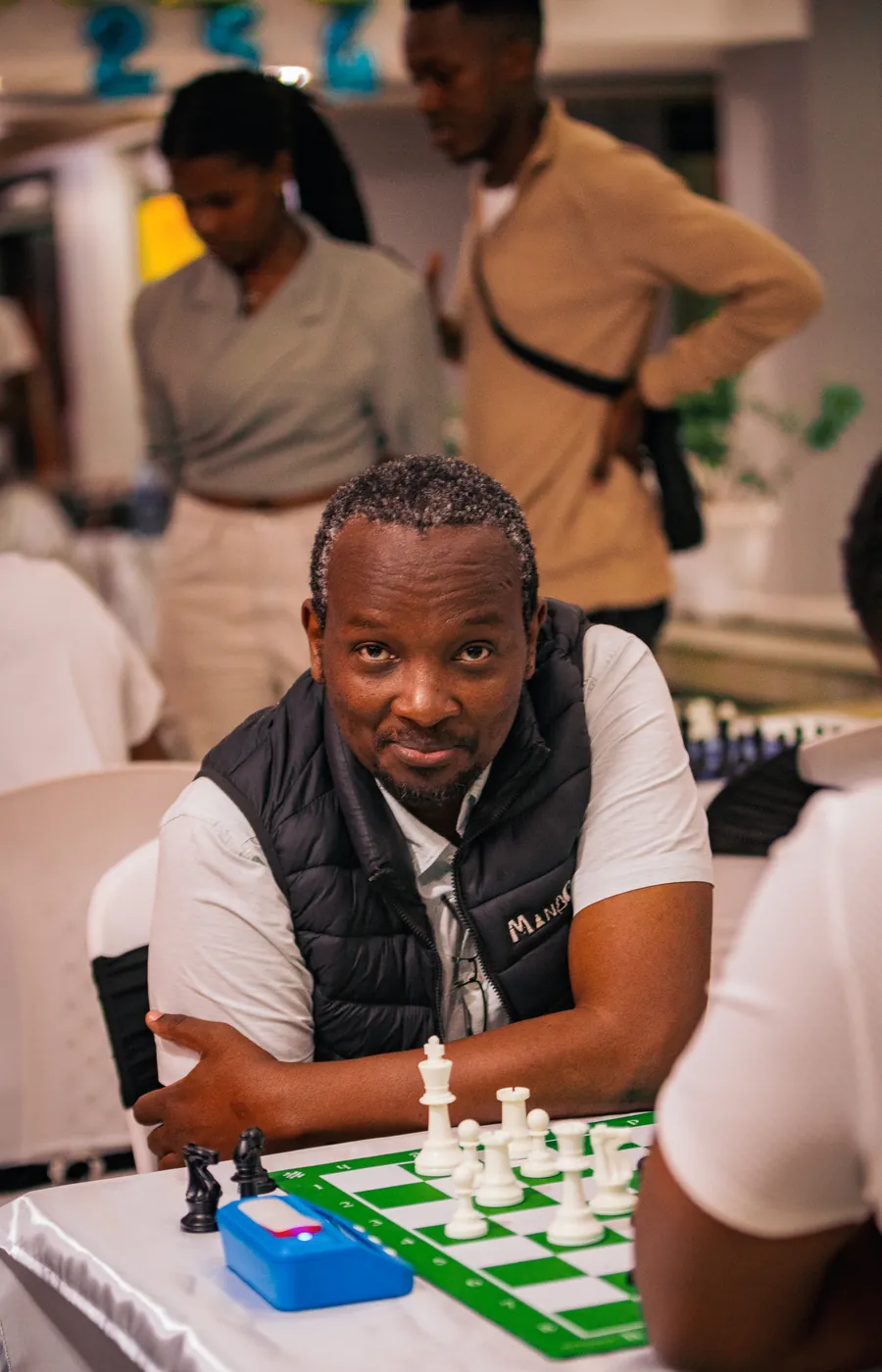 A player in a navy gilet at a green and white tournament board in the Chess254 clubhouse